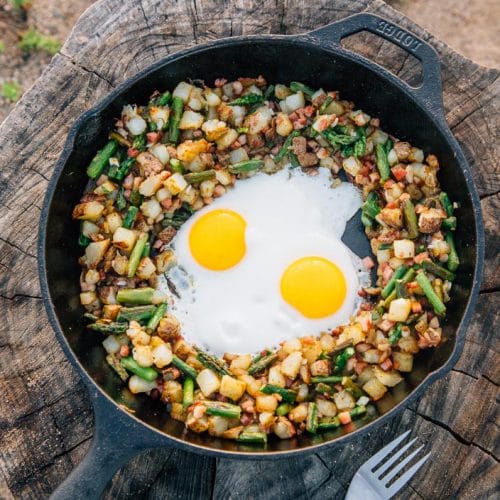 Potatoes, asparagus, and two eggs in a skillet on a stump