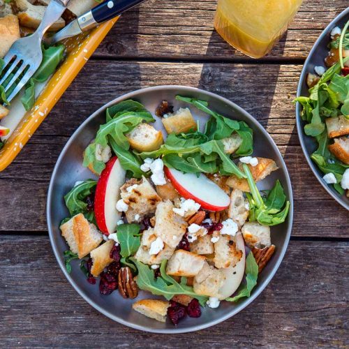 Two plates filled with panzanella salad next to a serving dish