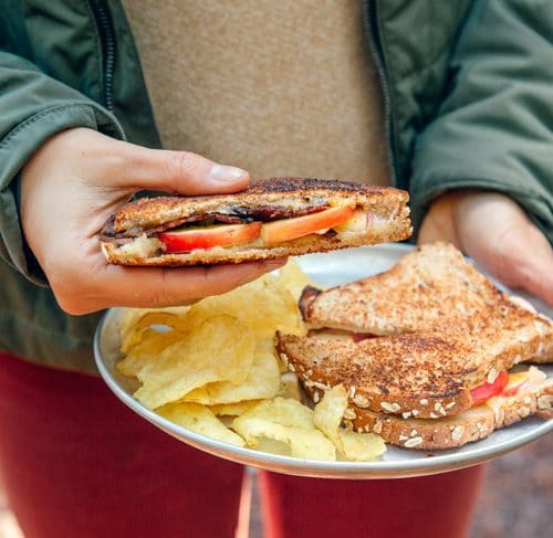 Megan holding a plate with grilled cheese and chips. She is holding one of the sandwiches.