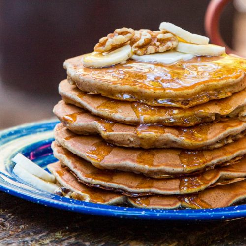 A stack of pancakes on a blue plate, topped with slices of bananas and walnuts.