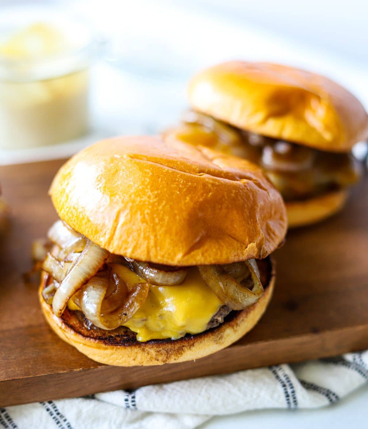 Burger patties and cheese in a bun on a wooden cutting board.