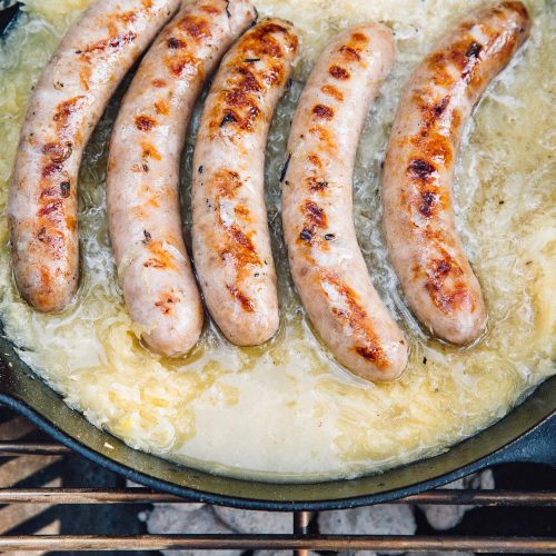 Beer brats simmering in beer and sauerkraut in a cast iron skillet