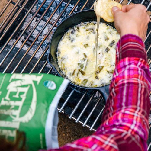 Dipping a chip into a skillet of queso fundido on a campfire.