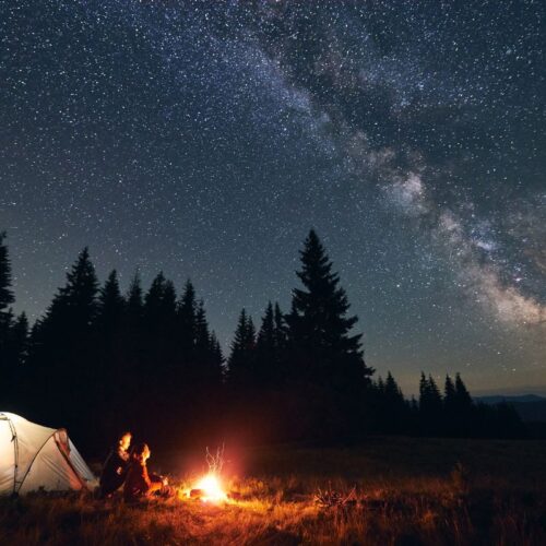 A couple sits next to a tent and a campfire under a starry sky