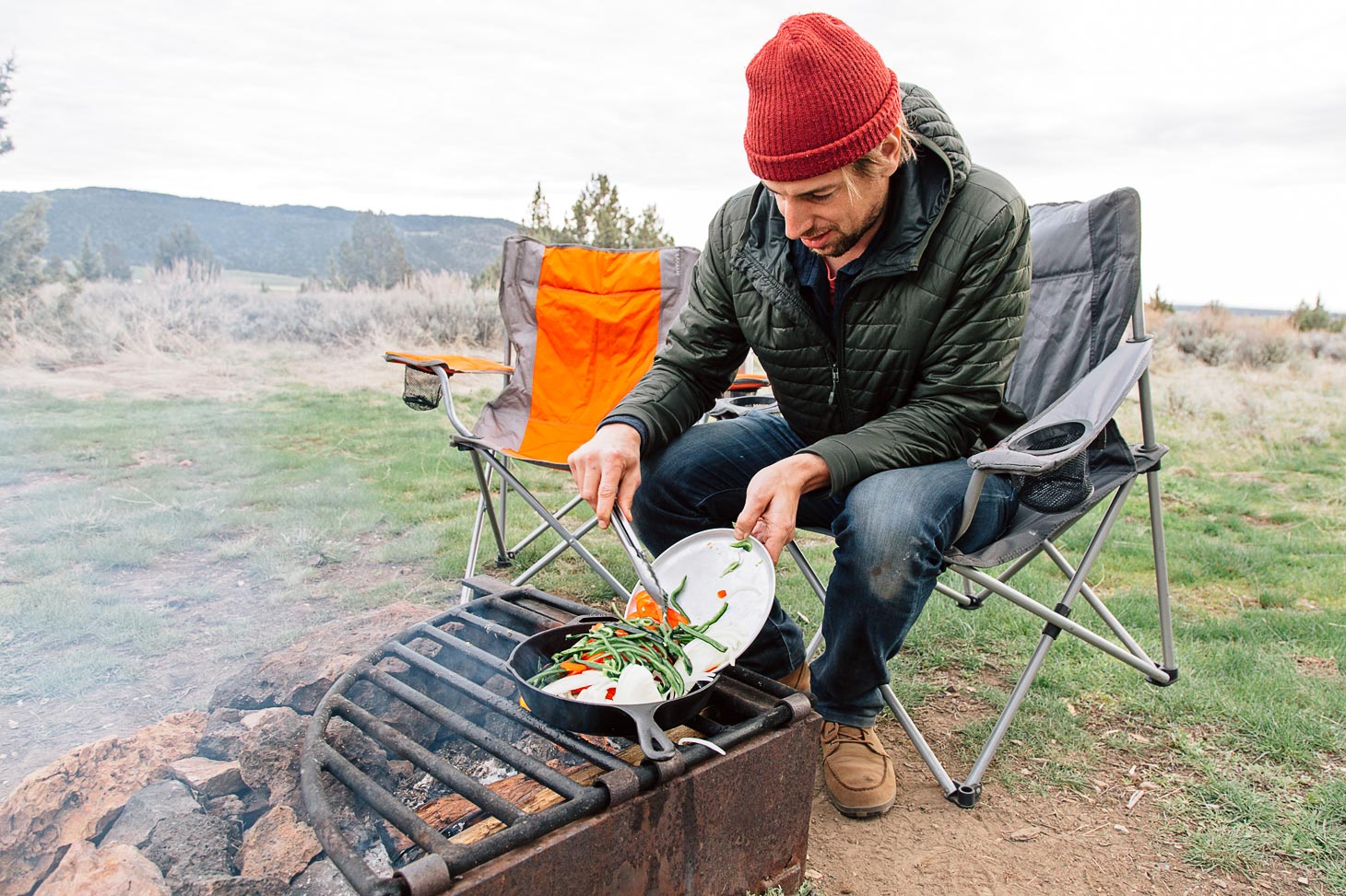 Michael adding sliced peppers into a cast-iron skillet over a campfire