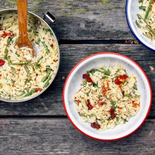 Overhead view of asparagus orzo in a camping bowl on a picnic table
