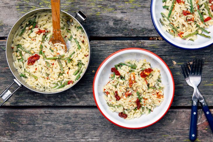 Overhead view of asparagus orzo in a camping bowl on a picnic table