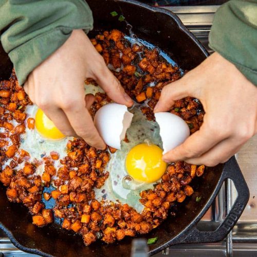 Megan cracking an egg into a skillet of sweet potato breakfast hash