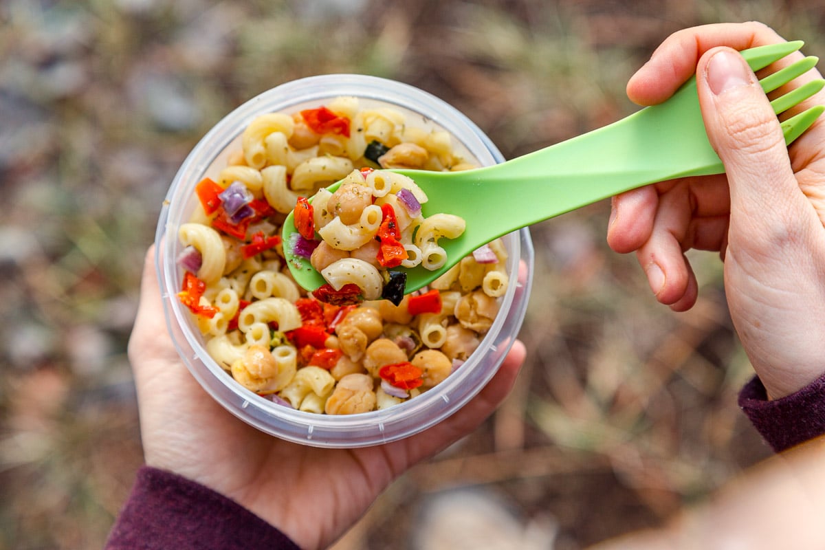 Megan holding a plastic container full of pasta salad. She's picking up a spoonful.