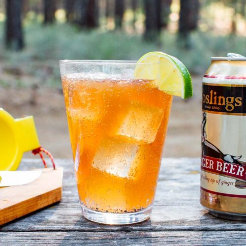 Dark and stormy in a clear glass. A bottle of rum and can of ginger beer are in frame.