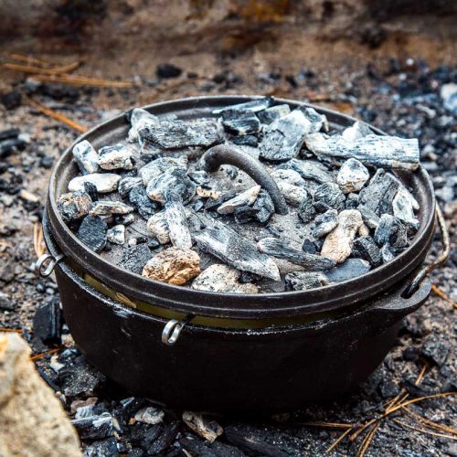 Dutch oven in a fire pit with embers on the lid