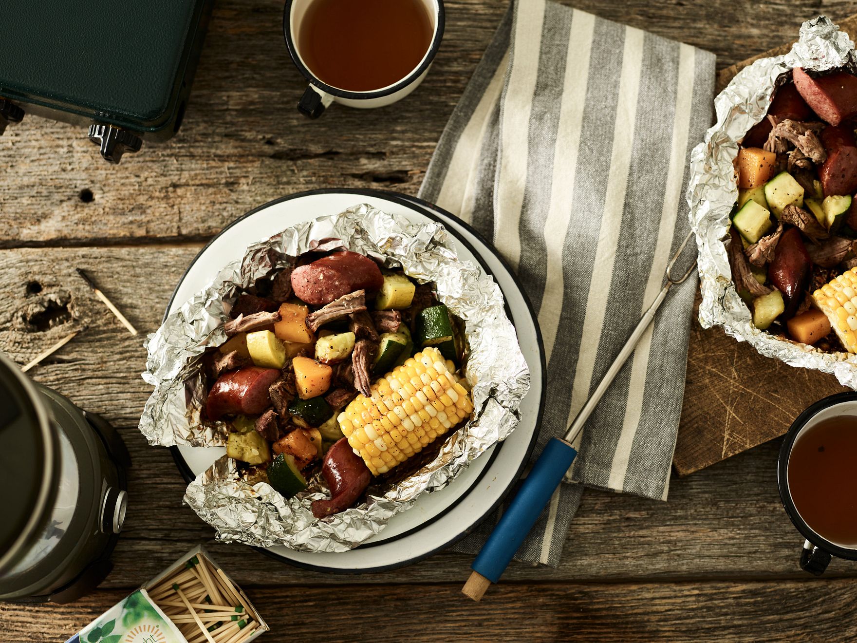 Beef with vegetables in a foil packet on a wood camp table.