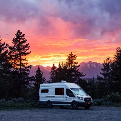 A campervan parked with a sunset and the Teton mountains in the background