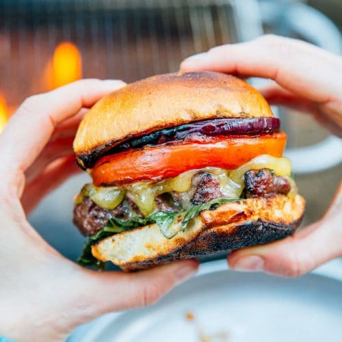 A woman holding a grilled burger in front of a campfire