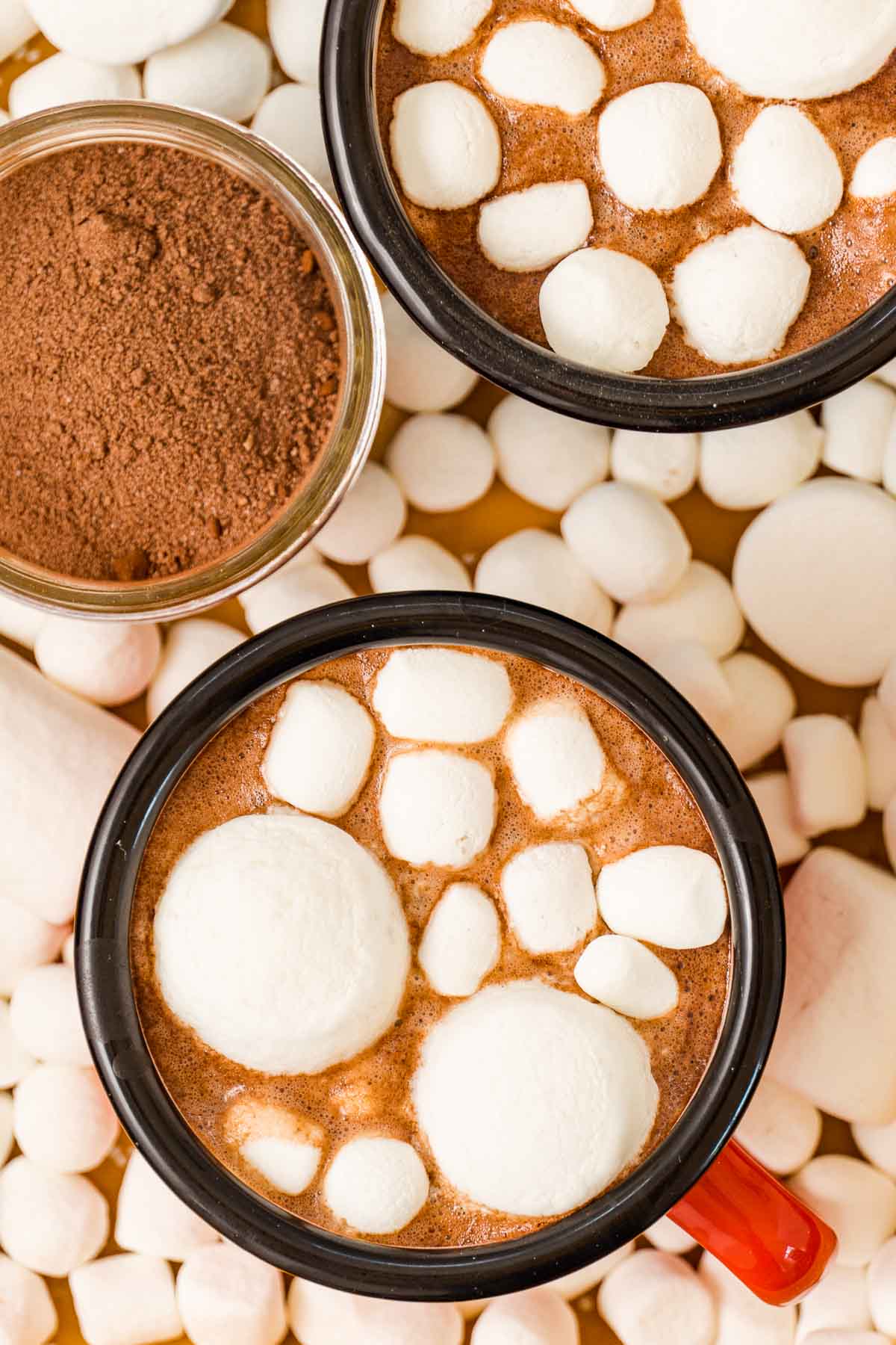 A close-up of two mugs of marshmallow-topped hot cocoa.