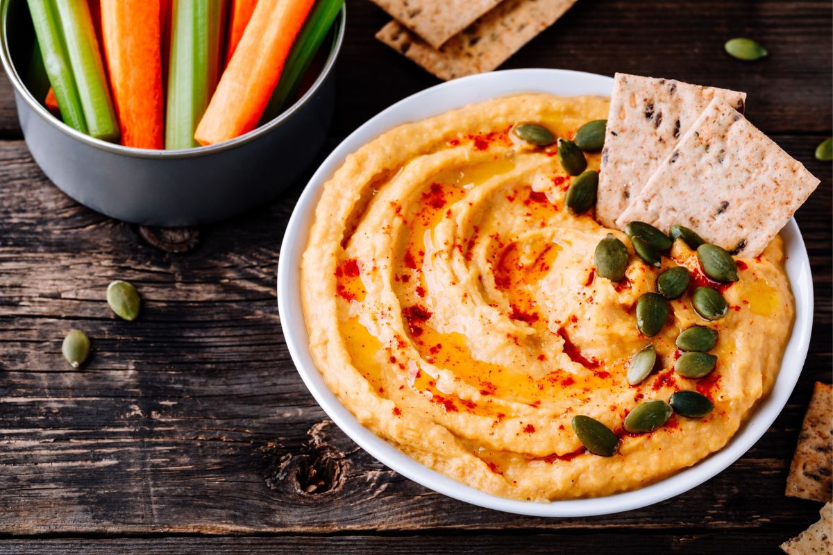Hummus in a bowl with veggie sticks and crackers.