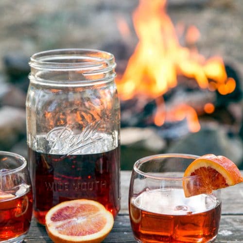 Negroni cocktail in a mason jar on a table in front of a campfire.