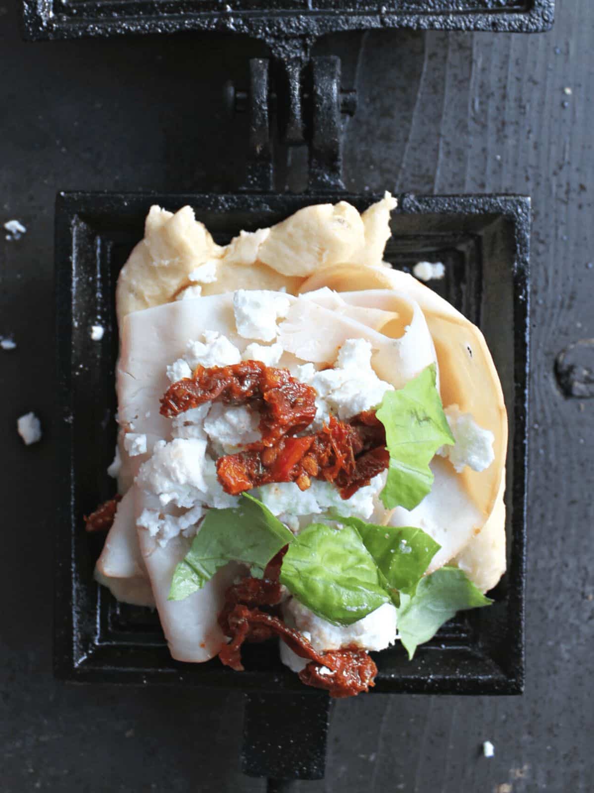 Croissant in a pie iron layered with meat, tomatoes, and greens.