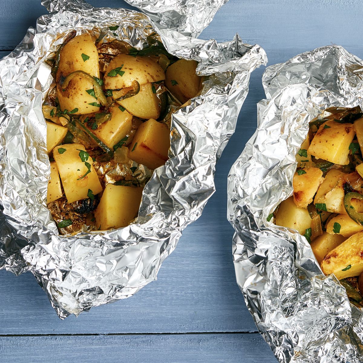 Potatoes and poblano peppers in foil on a wood table.