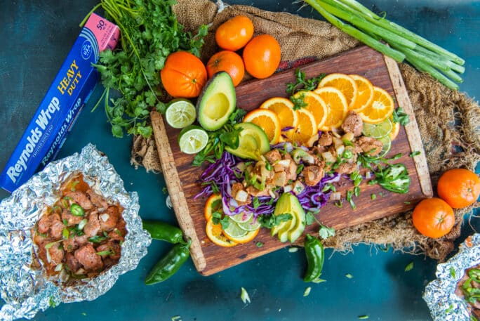 Chunks of pork surrounded with sliced citrus on a wood cutting board.