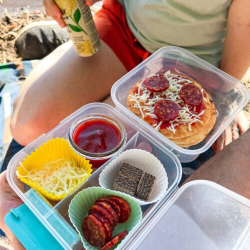 Megan sitting on a picnic blanket and Michael is holding a snack box on his lap