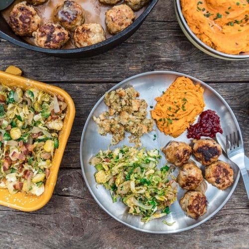 A plate filled with meatballs, brussels sprouts, and sweet potatoes on a table surrounded by serving dishes
