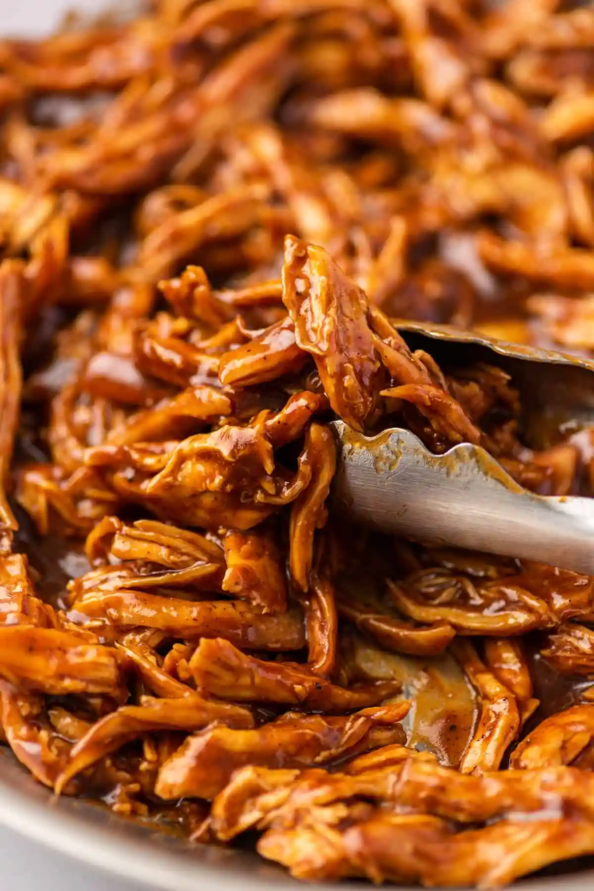 A serving spoon scoops up a portion of sticky, caramelized shredded chicken, highlighting the glazed texture and sauce-coated meat strands.