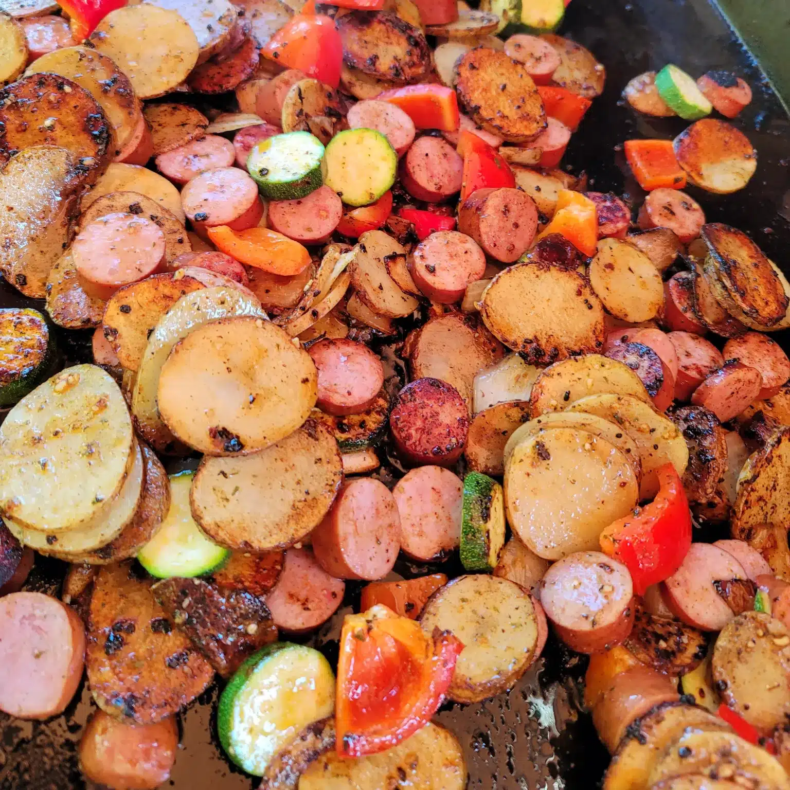 Sausages potatoes and zucchini on a griddle.